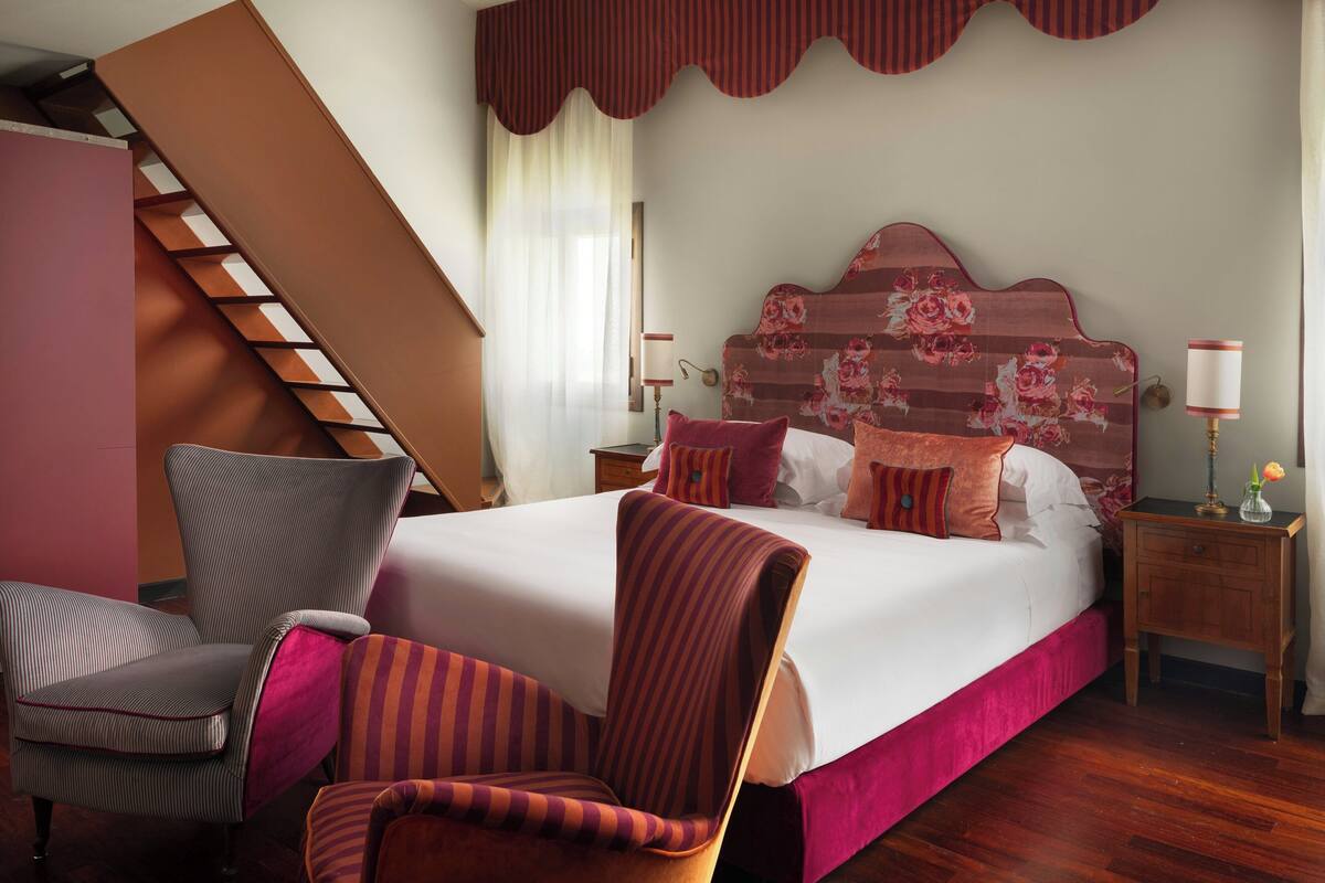 Un dormitorio con una cama grande, una silla, una mesita de noche, una lámpara y una escalera.