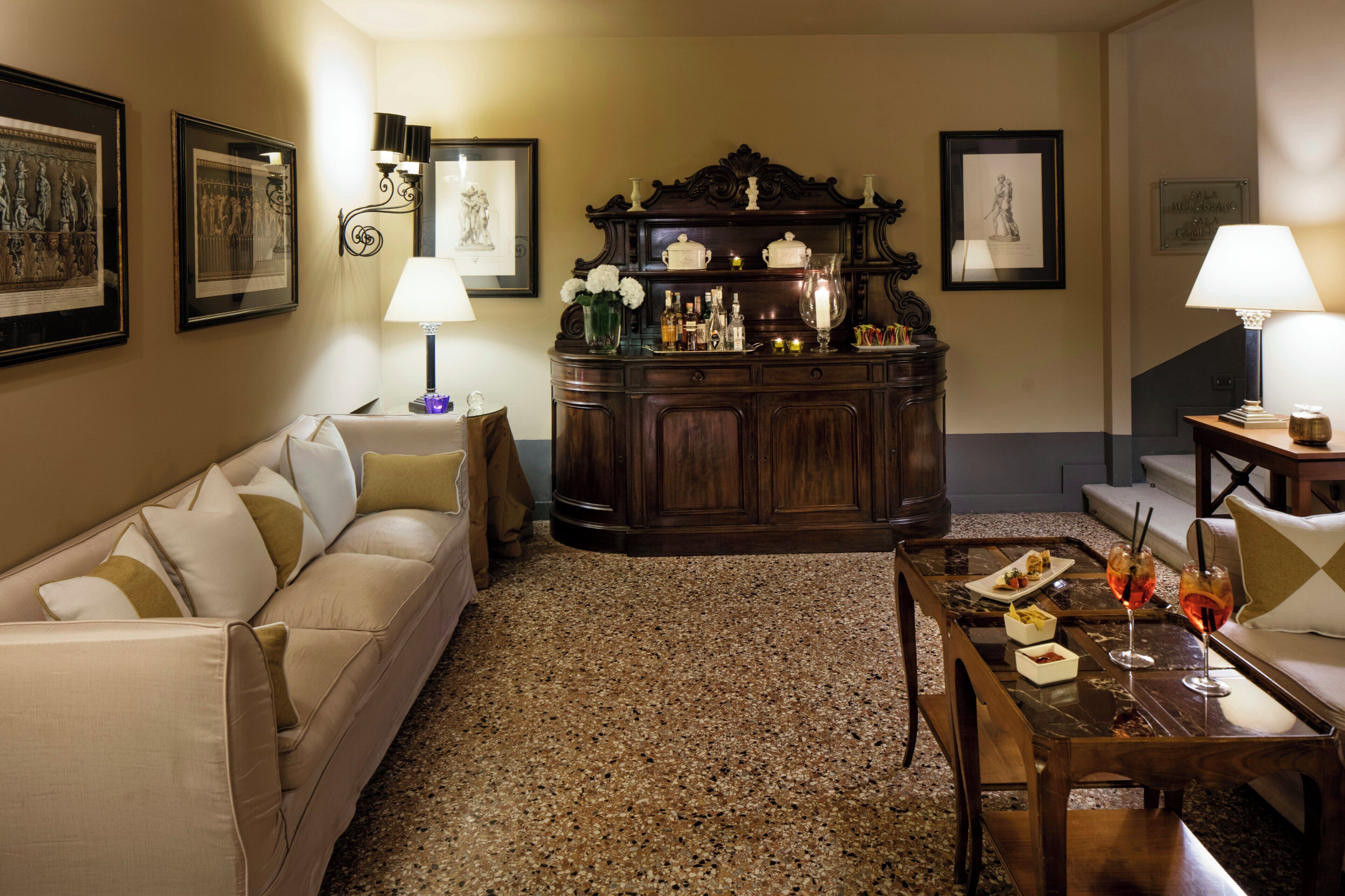 A living room with a sofa, a coffee table with drinks, a cabinet with decorative items, and framed pictures on the walls.