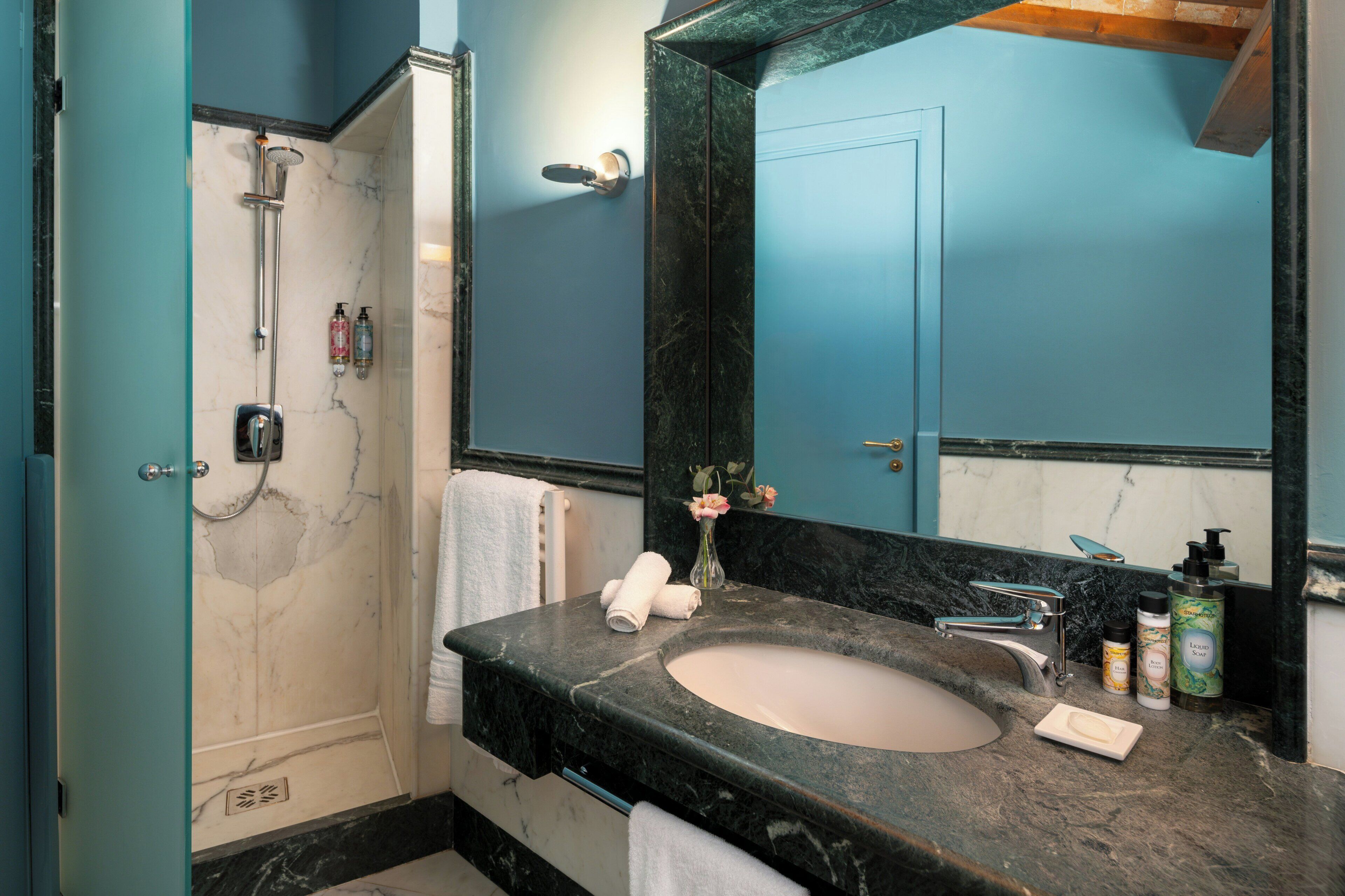 A bathroom with a marble sink, a large mirror, a shower, and a towel rack.