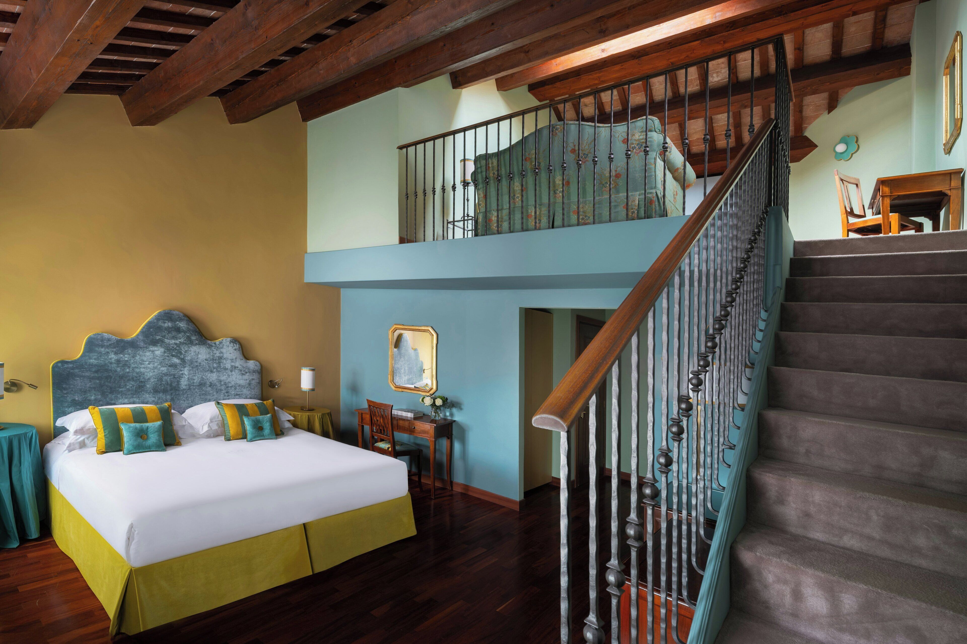 Ein Schlafzimmer mit Bett, Schreibtisch, Stuhl, einer Treppe und einem Balkon.