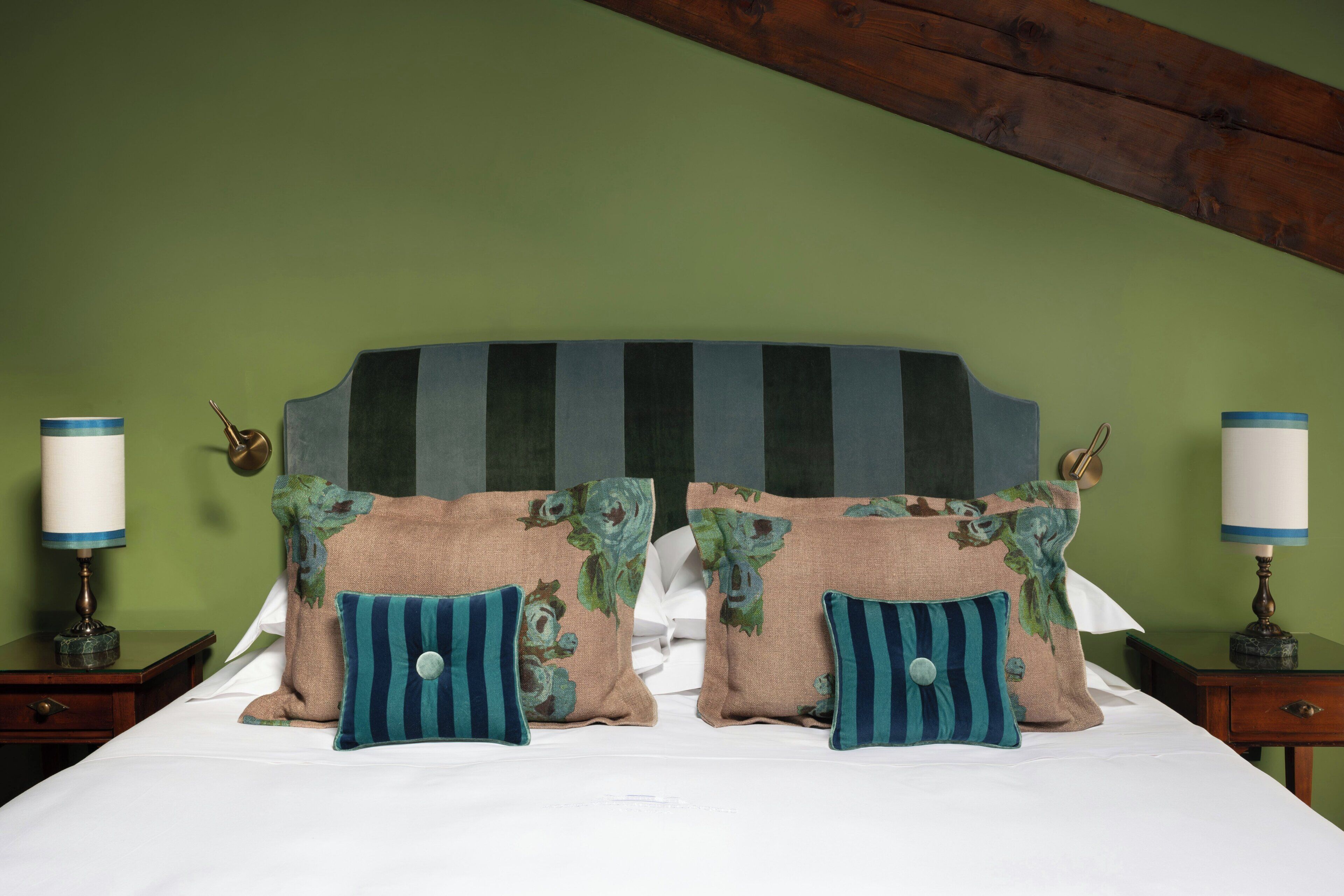 Una cama con cabecera a rayas, almohadas florales y lámparas de noche.