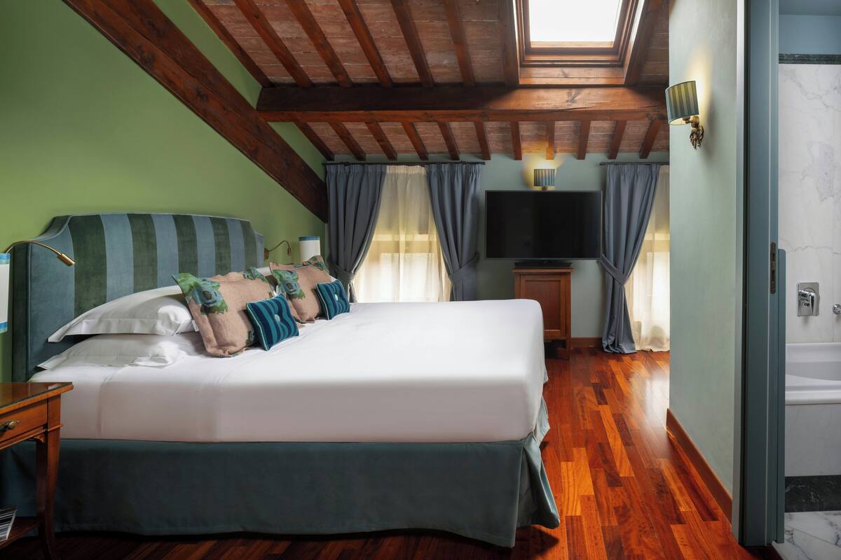 Un dormitorio con una cama grande, televisión, techo de madera y puerta de baño.