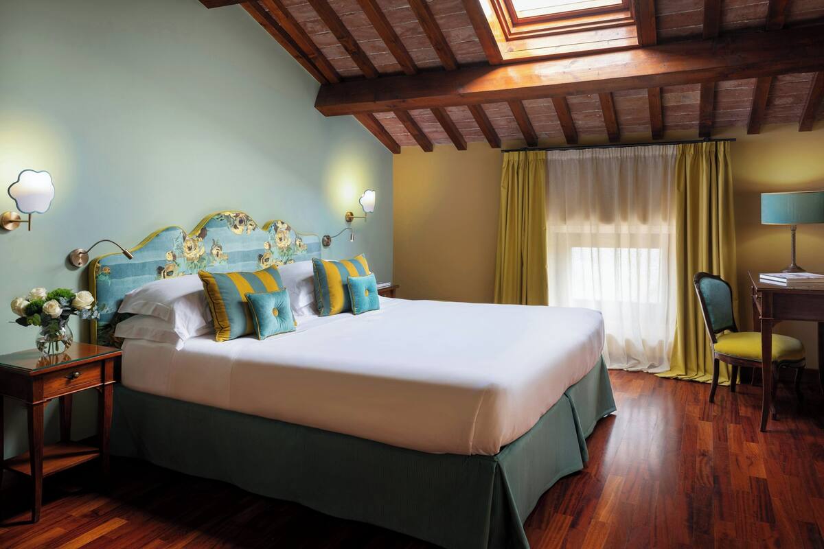 Un dormitorio ordenado con una cama grande, un escritorio y una silla, con suelo de madera y techo inclinado.