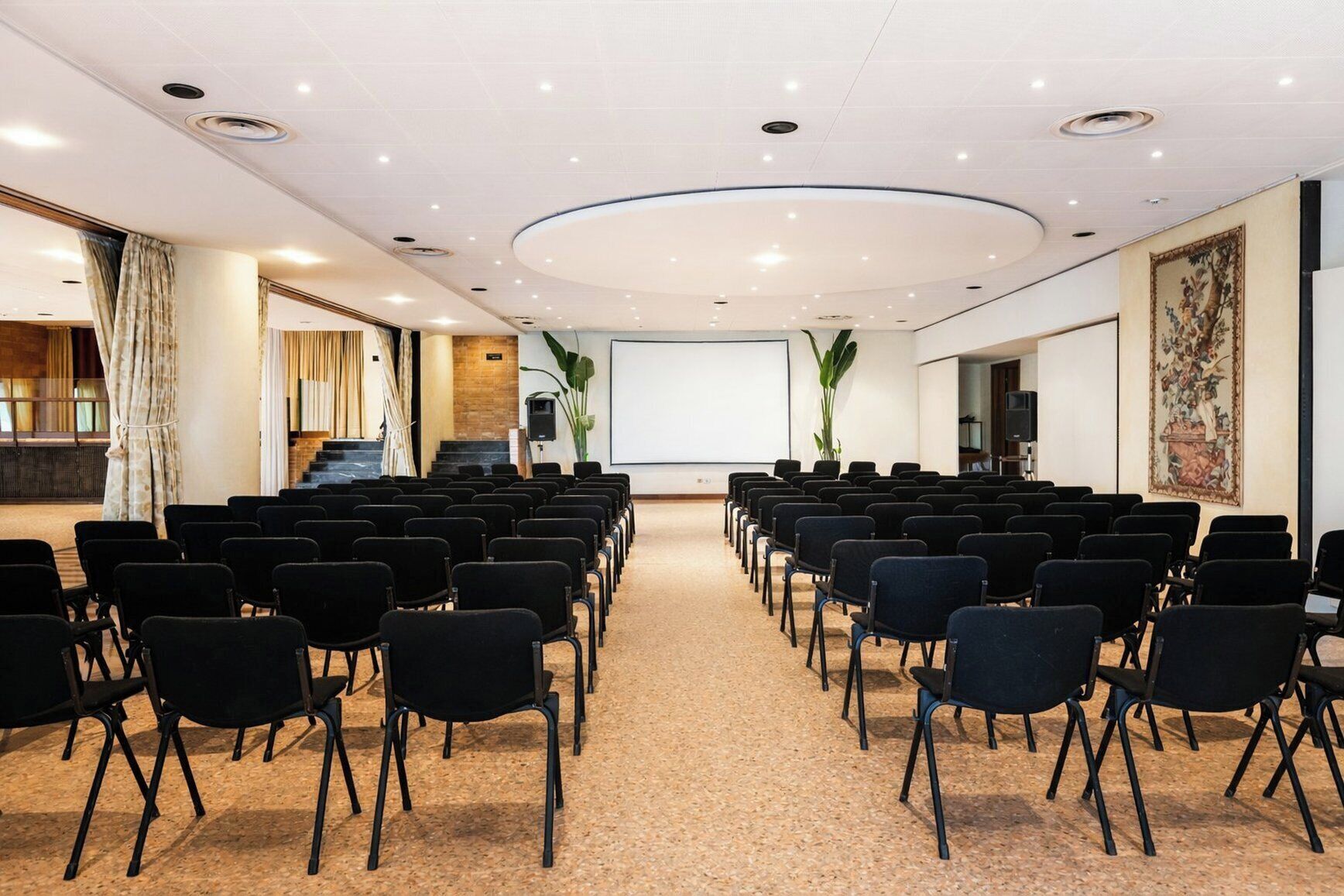 A conference room with rows of black chairs, a large screen, and a carpeted floor.