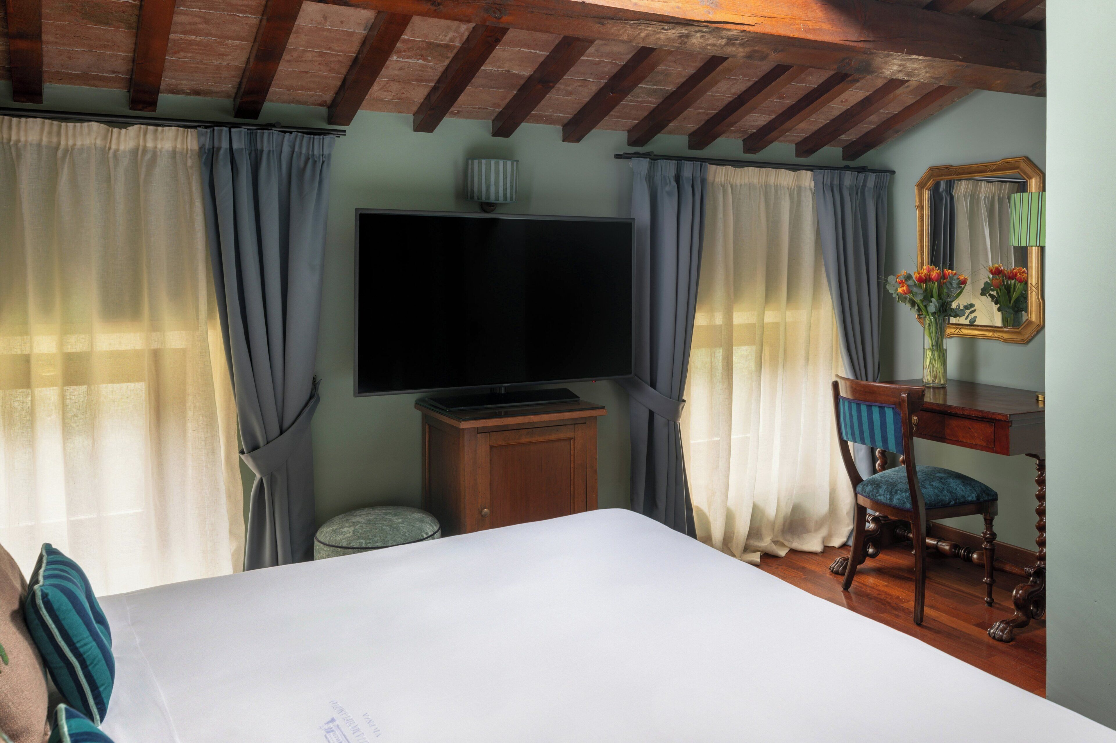 Quarto com cama, televisão, armário de madeira, cadeira e espelho.