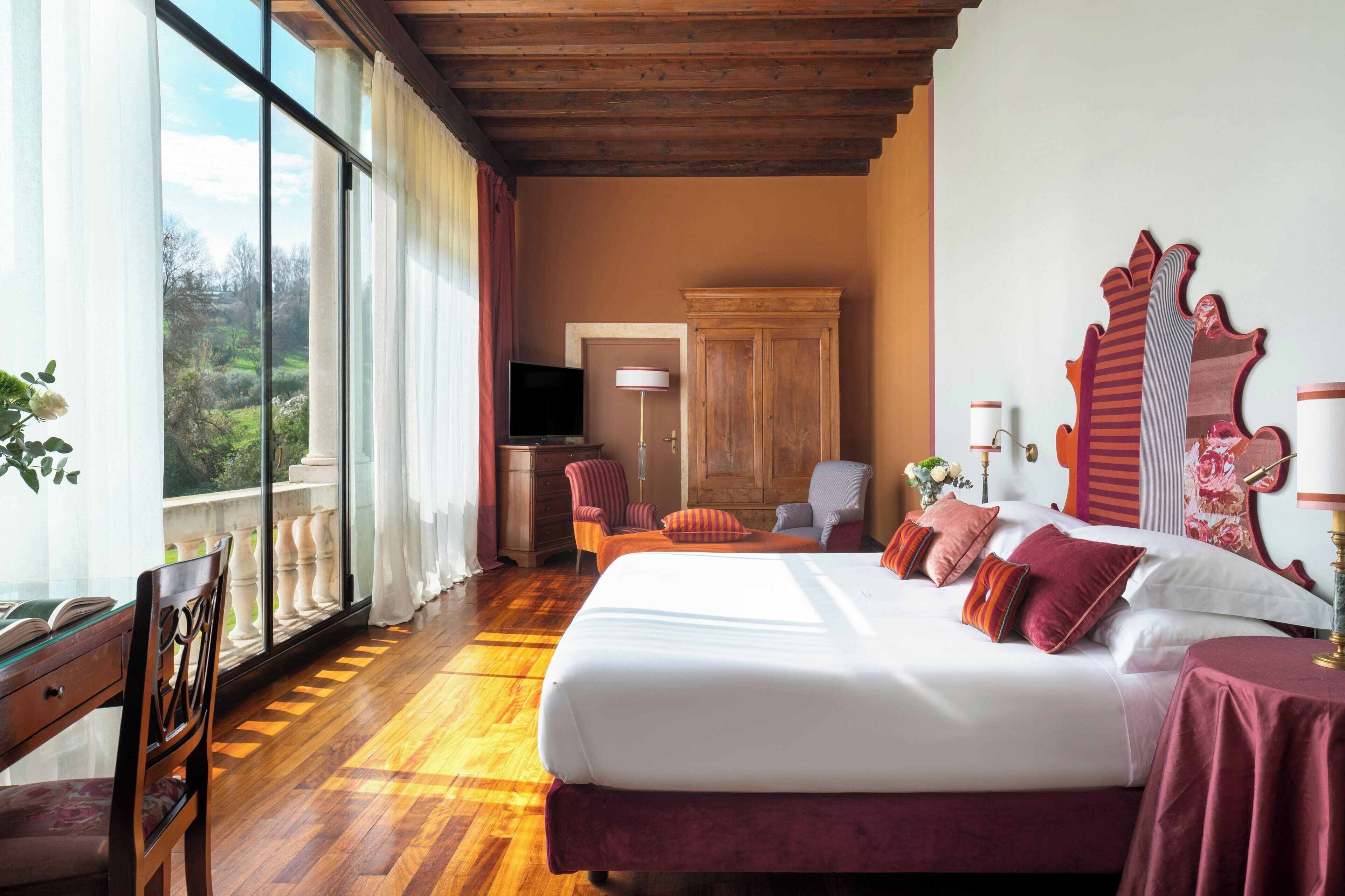 A hotel room with a large bed, a television, a desk, and a view of the outdoors.