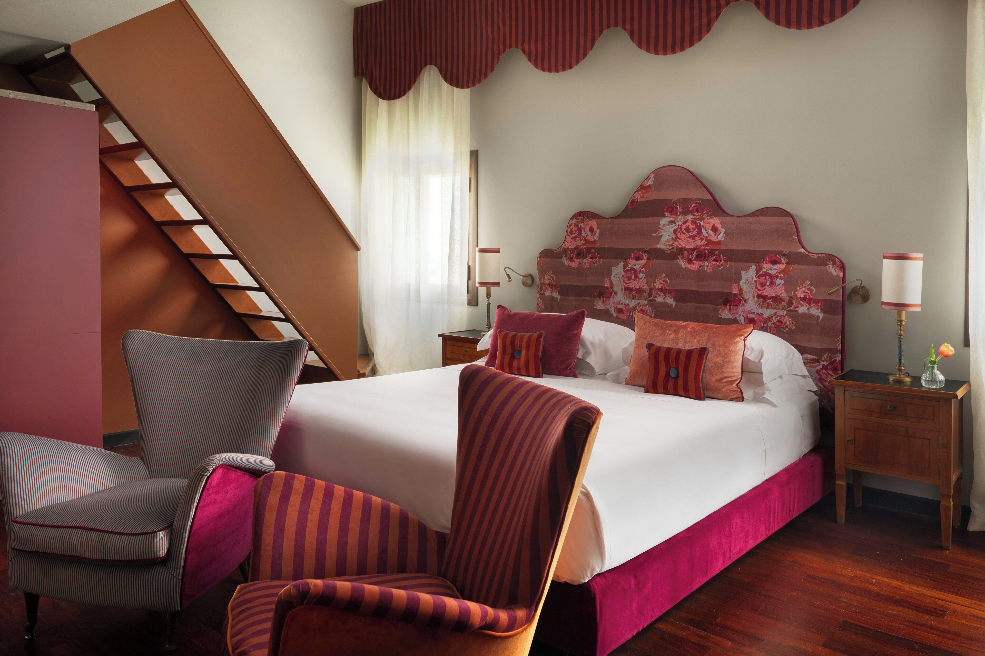 Une chambre à coucher avec un grand lit, une chaise, une table de chevet, une lampe et un escalier.