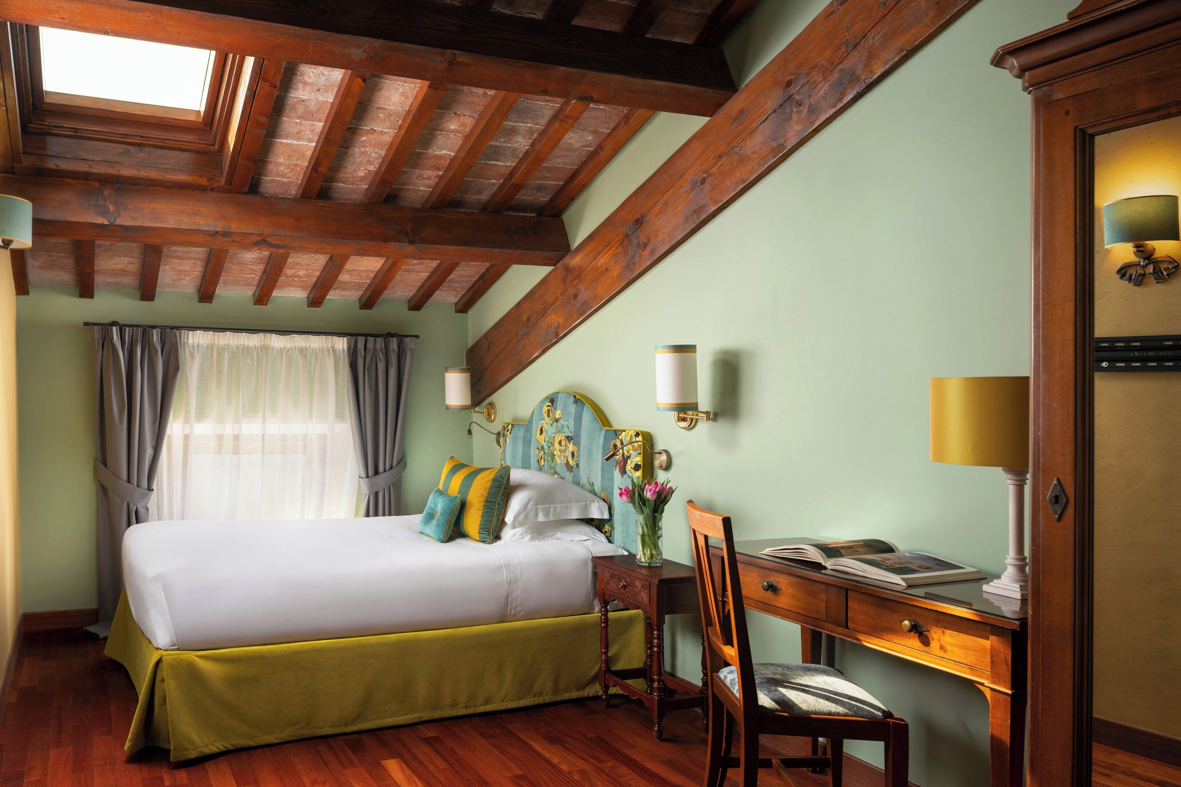 A bedroom with a bed, a desk, a chair, a lamp, and a window with curtains.