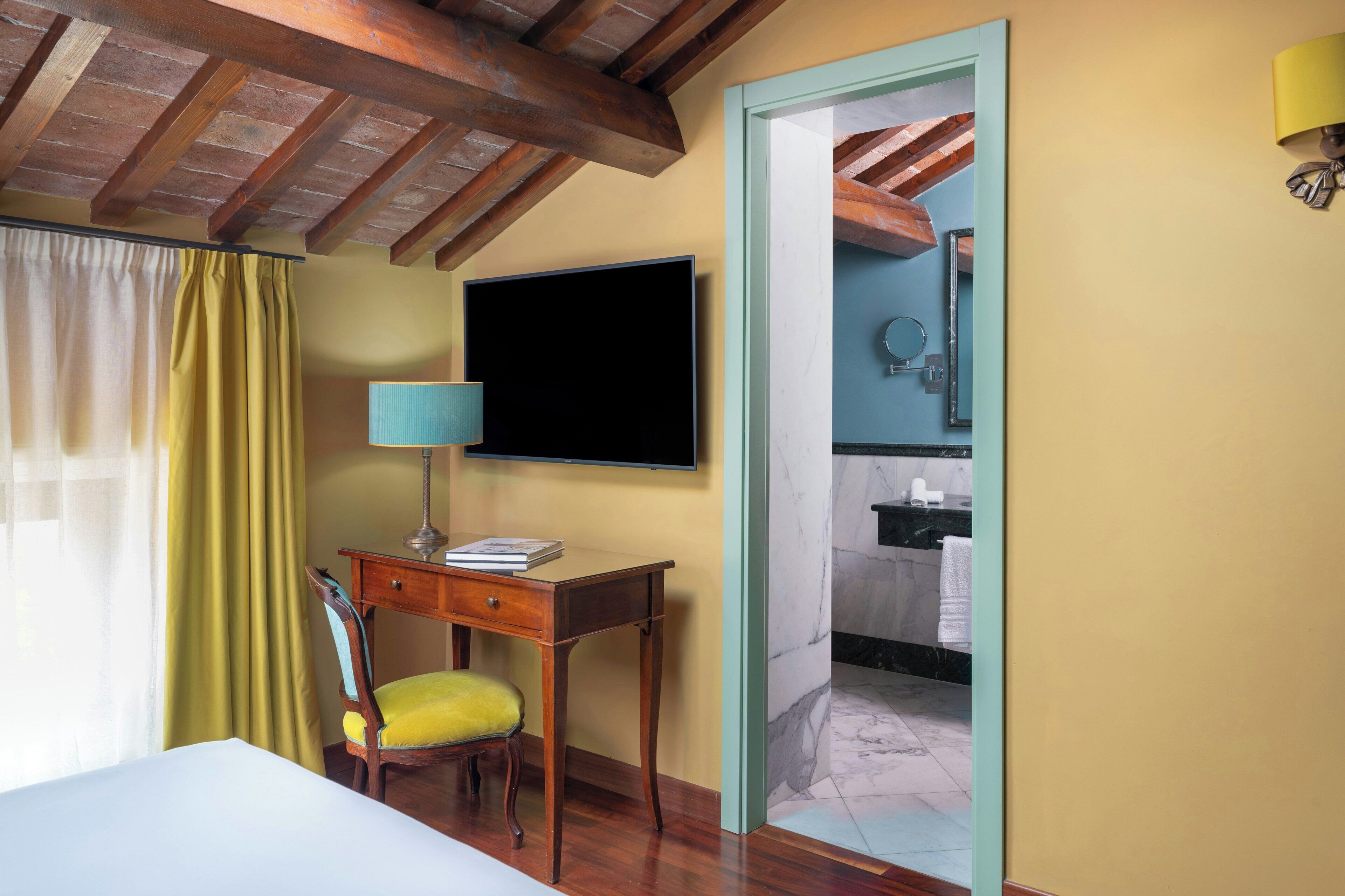 Une pièce comprenant un lit, un bureau avec une chaise, une télévision et une salle de bain visible à travers une porte ouverte.