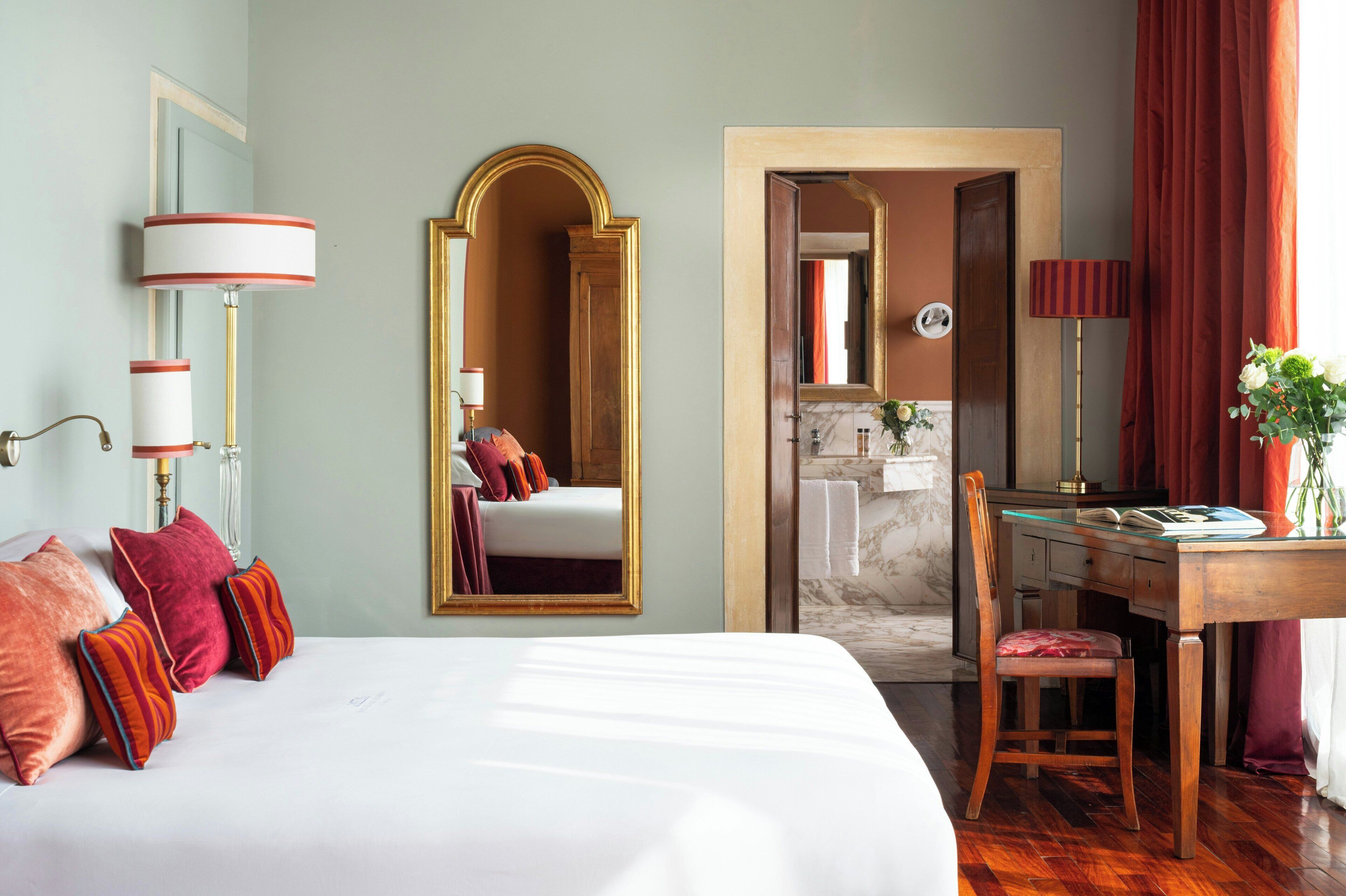 A hotel room with a bed, a desk, a chair, a mirror, and a bathroom visible through an open door.