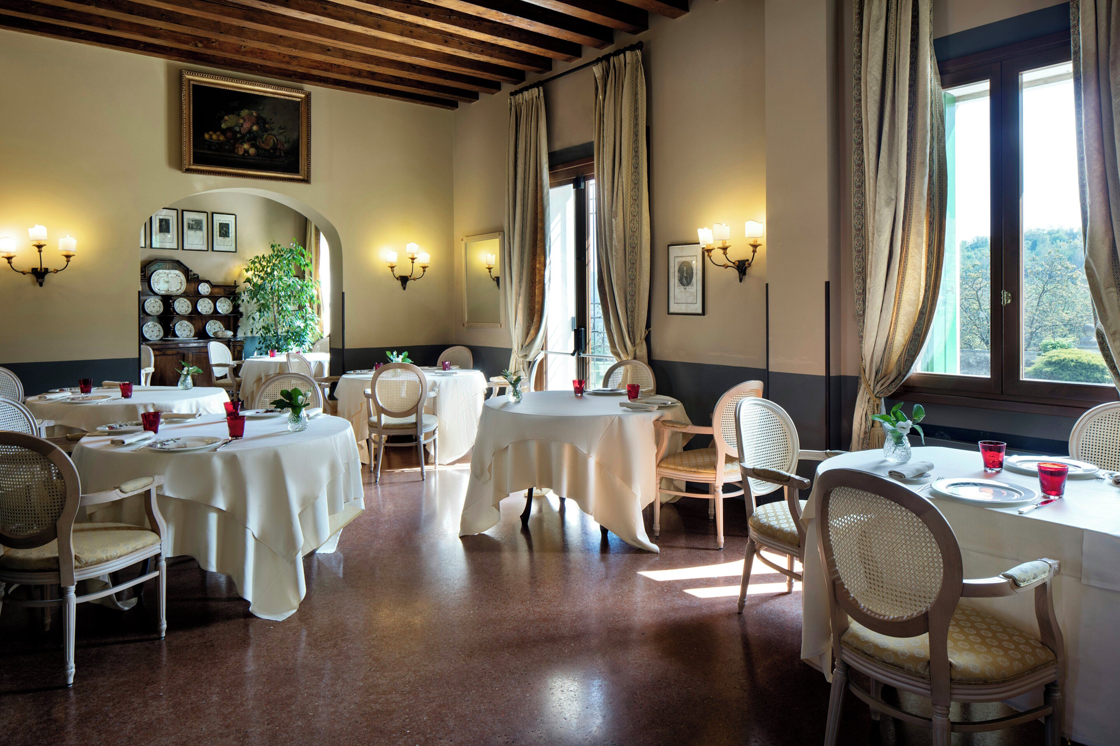 Un comedor con mesas redondas, sillas e iluminación fijada a la pared.