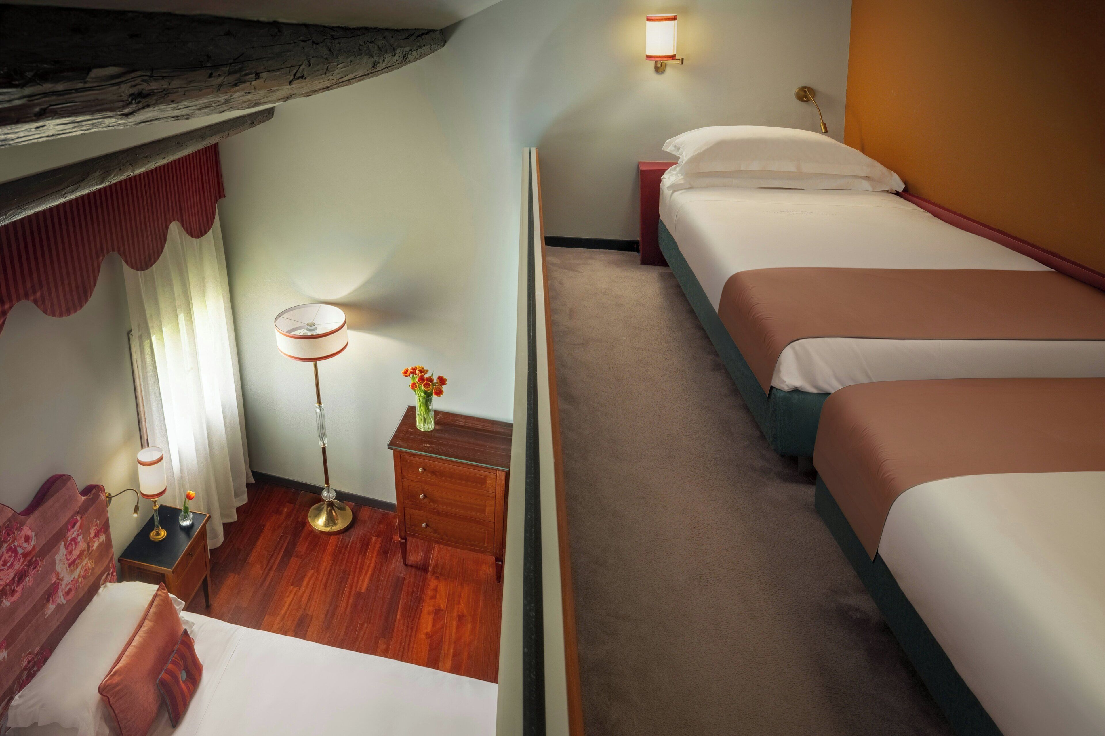 A hotel room with a wooden ceiling, a single bed, a nightstand with a lamp, and a small table with a vase of flowers.