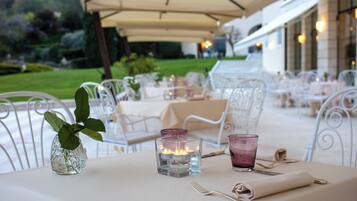 Un área de comedor al aire libre con sillas y mesas de metal blanco, velas y un jarrón con una planta.