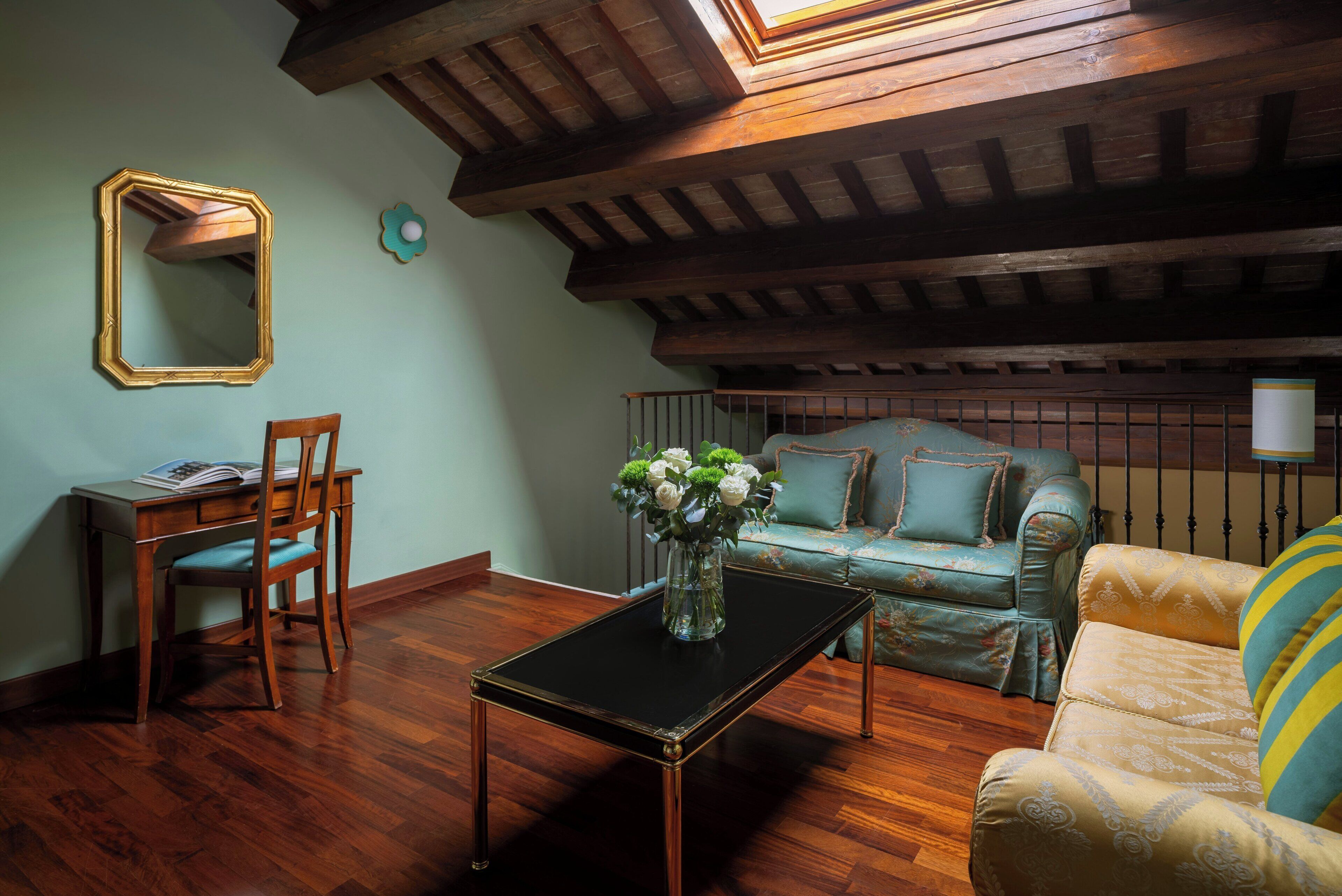 A room with a wooden ceiling, a sofa, a chair, a table with a vase, and a mirror.