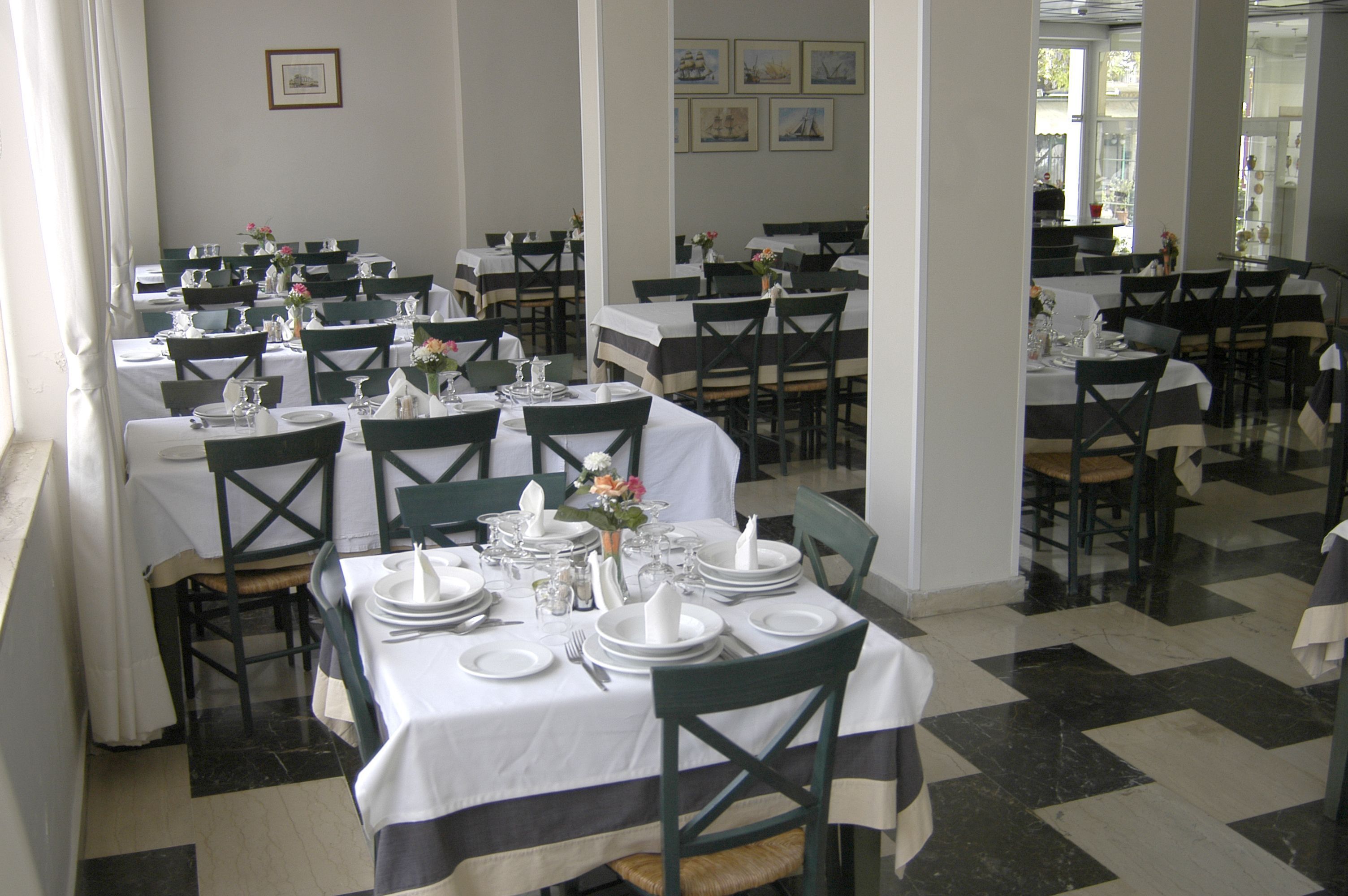 Une salle à manger avec plusieurs tables dressées pour le service, chacune étant recouverte d’une nappe blanche et entourée de chaises vertes.