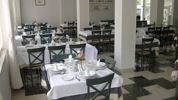 A dining area with multiple tables set for service, each with white tablecloths and green chairs.