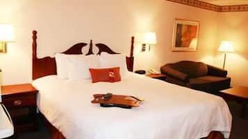 A hotel room with a large bed, a wooden headboard, two bedside tables with lamps, a brown armchair, and a painting on the wall.