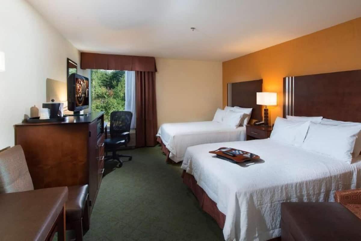 A hotel room with two beds, a desk, a chair, and a TV.