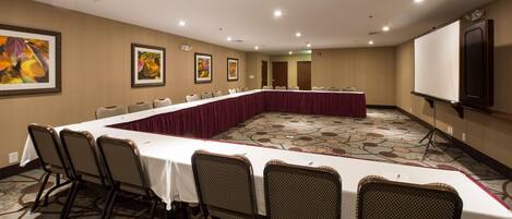 A conference room with a long table, chairs, a projector screen, and framed artwork on the walls.