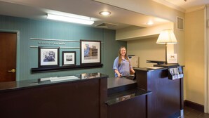 A reception desk with a "Welcome to Cornellia" sign, framed pictures, and a lamp. - Hampton Inn Cornelia (Cornelia)