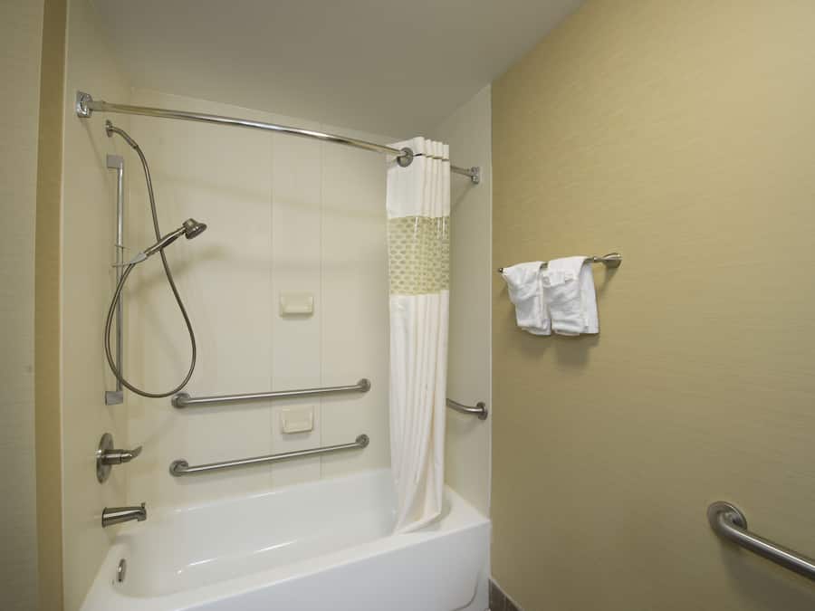 A bathroom with a bathtub, shower, and handrails.