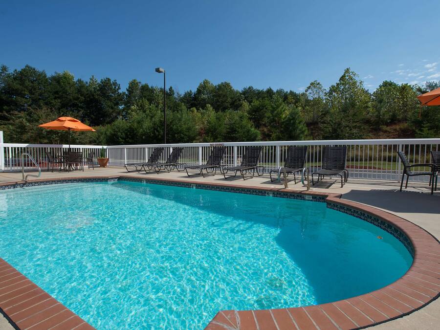 A clear blue swimming pool with a white fence and lounge chairs around it.