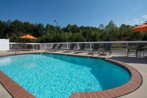 A clear blue swimming pool with a white fence and lounge chairs around it.