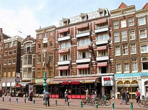 Une rangée de bâtiments de style européen traditionnel, à plusieurs étages, dotés de balcons et de marquises rouges.