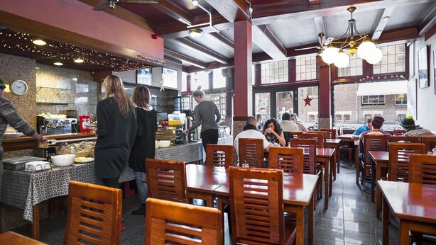 A restaurant with wooden tables and chairs, a kitchen area, and large windows. - Delta Hotel City Center (Amsterdam)