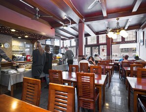 A restaurant with wooden tables and chairs, a kitchen area, and large windows. - Delta Hotel City Center (Amsterdam)