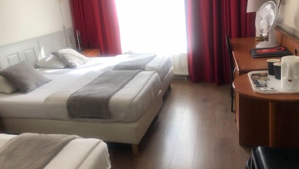 A hotel room with two beds, a desk with a lamp, a coffee maker, and a window with red curtains. - Delta Hotel City Center (Amsterdam)