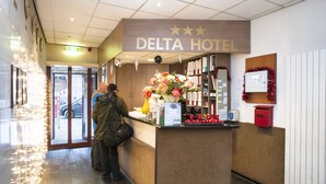 A hotel reception area with a sign reading "DELTA HOTEL," a counter with a vase of flowers, a mail box, and a bulletin board. - Delta Hotel City Center (Amsterdam)