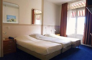 A hotel room with two beds, a bedside table, a mirror, and a window with curtains. - Delta Hotel City Center (Amsterdam)