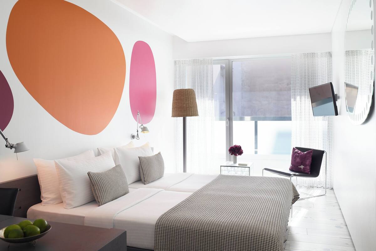 Un dormitorio moderno con una cama grande, una mesita de noche con un frutero, y una ventana con vistas.