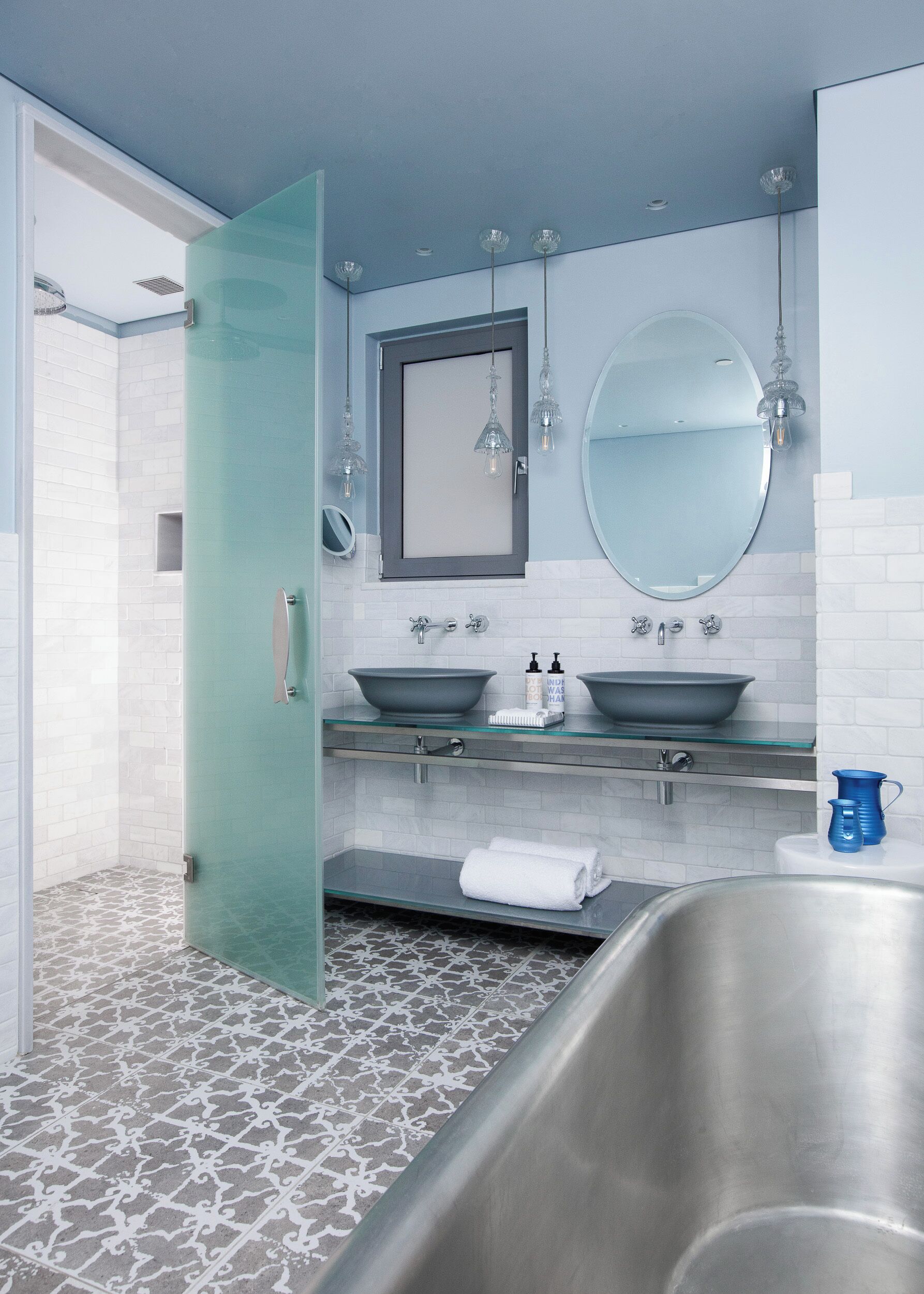 A modern bathroom with a glass shower enclosure, a double sink with a large mirror above, and a patterned floor.
