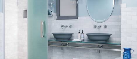 A modern bathroom with a glass shower enclosure, a double sink with a large mirror above, and a patterned floor.