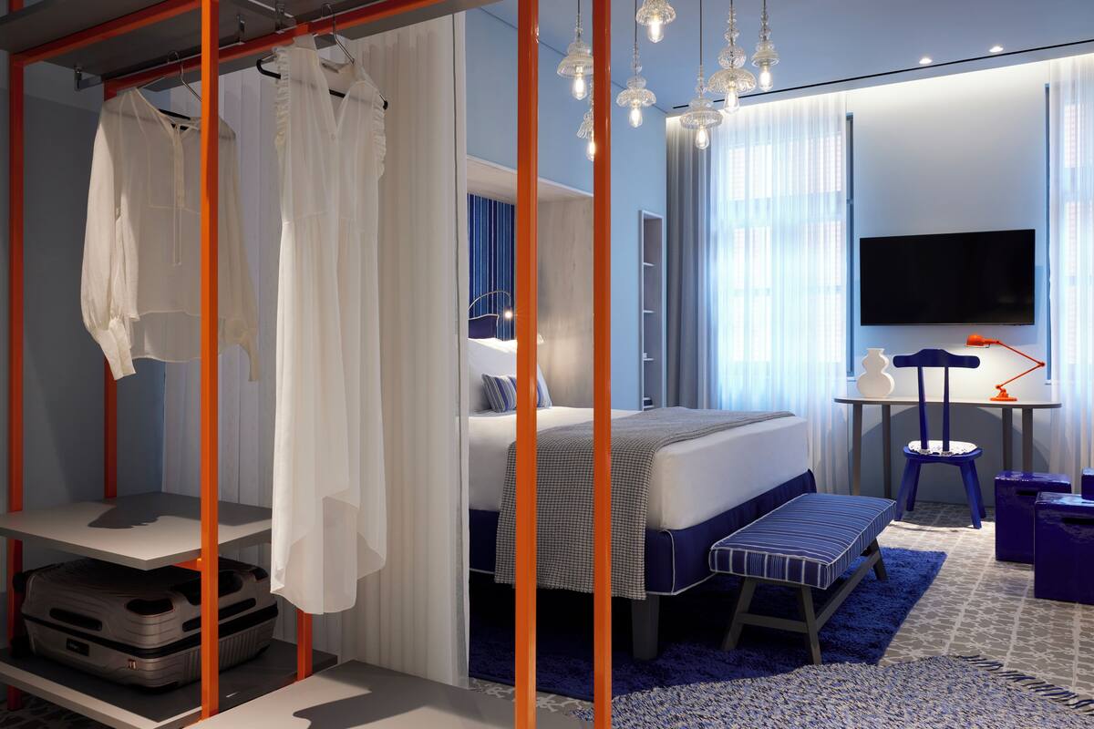 Una habitación de hotel moderna con cama, escritorio, televisor y armario.