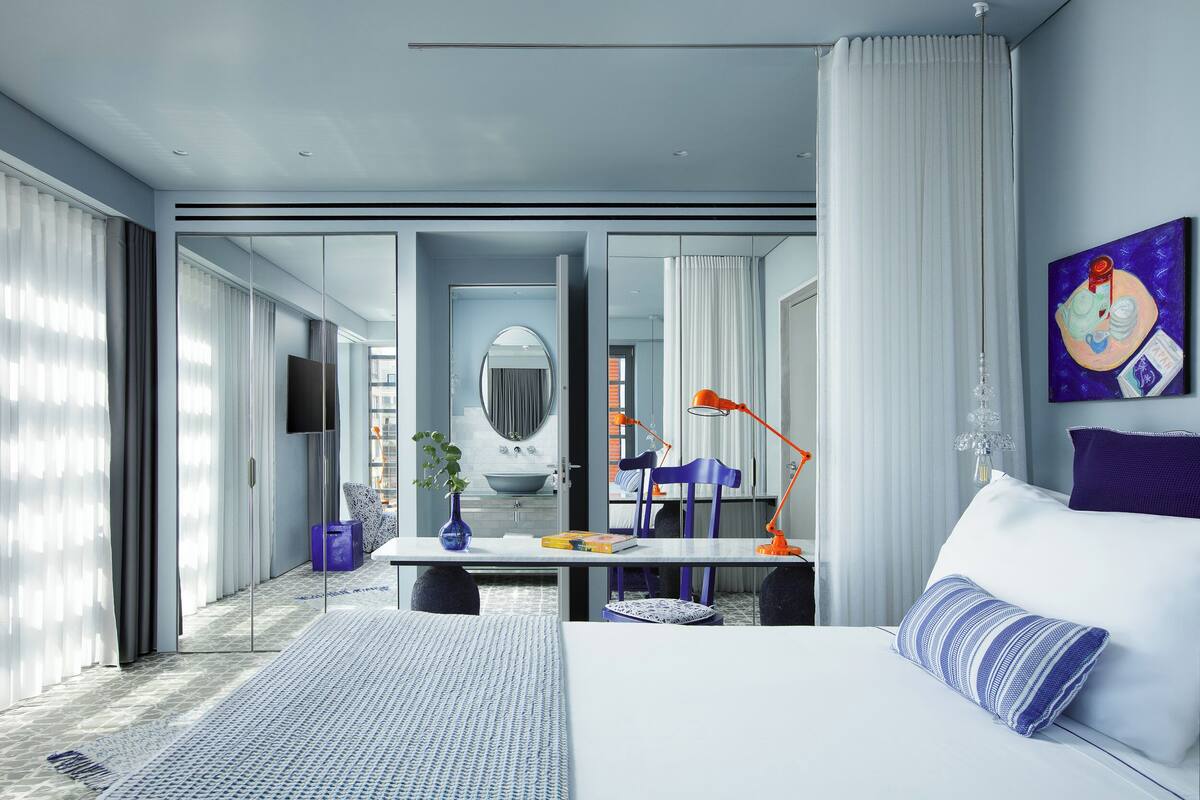 Habitación de hotel moderna con una cama grande, un escritorio con una silla, televisión y baño visible a través de una puerta de cristal.