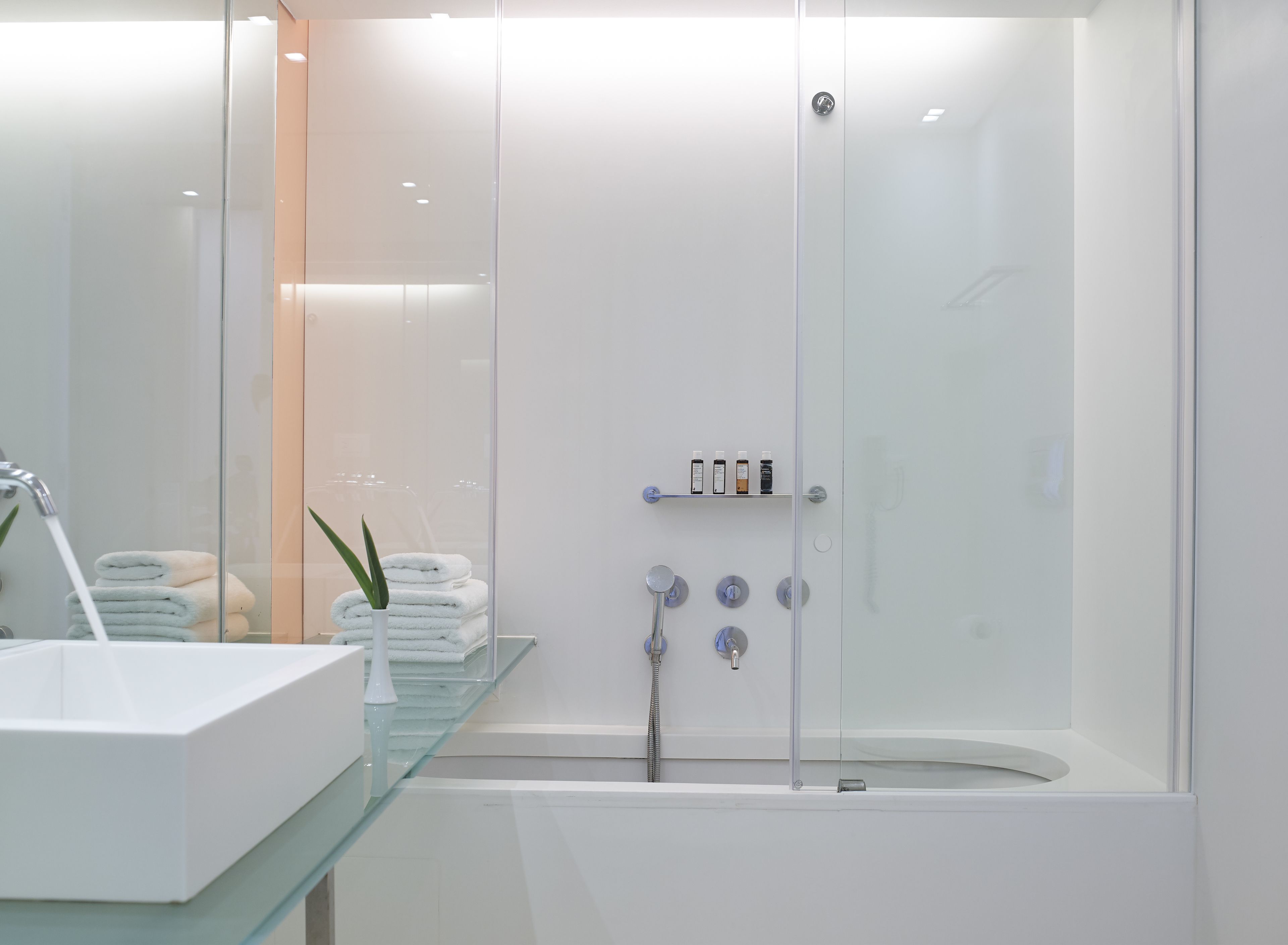 A modern bathroom with a glass-enclosed shower, a white bathtub, and a glass shelf with toiletries.