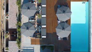 En vy från ovan av ett hotell med en swimmingpool, flera utomhusområden med sittplatser och parasoller samt en träterrass.