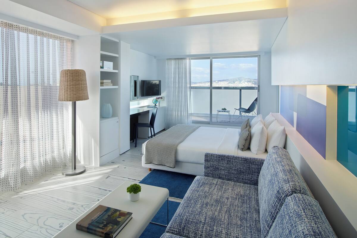 Una habitación de hotel moderna con una cama grande, un escritorio y un balcón con vistas.