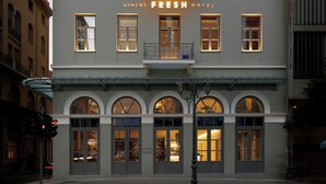 Ett hotell med en skylt som visar texten ”ATHENS FRESH HOTEL”. Det har flera fönster och en balkong med ett räcke.