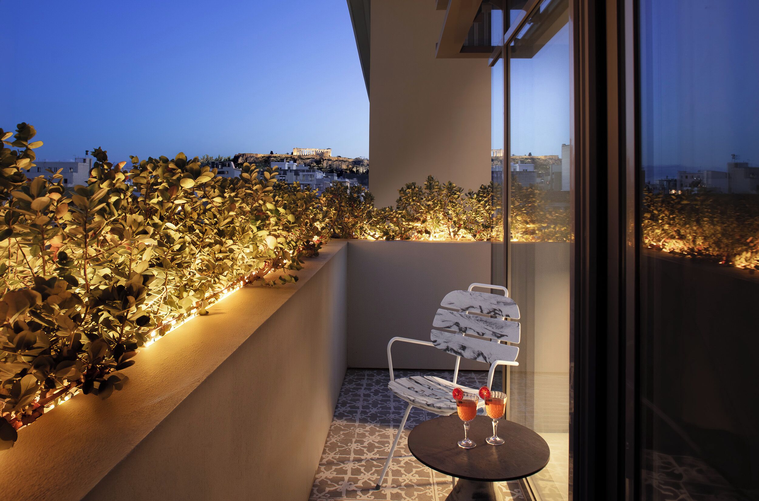 A balcony with a table and chairs, a view of the cityscape, and a plant-covered wall.