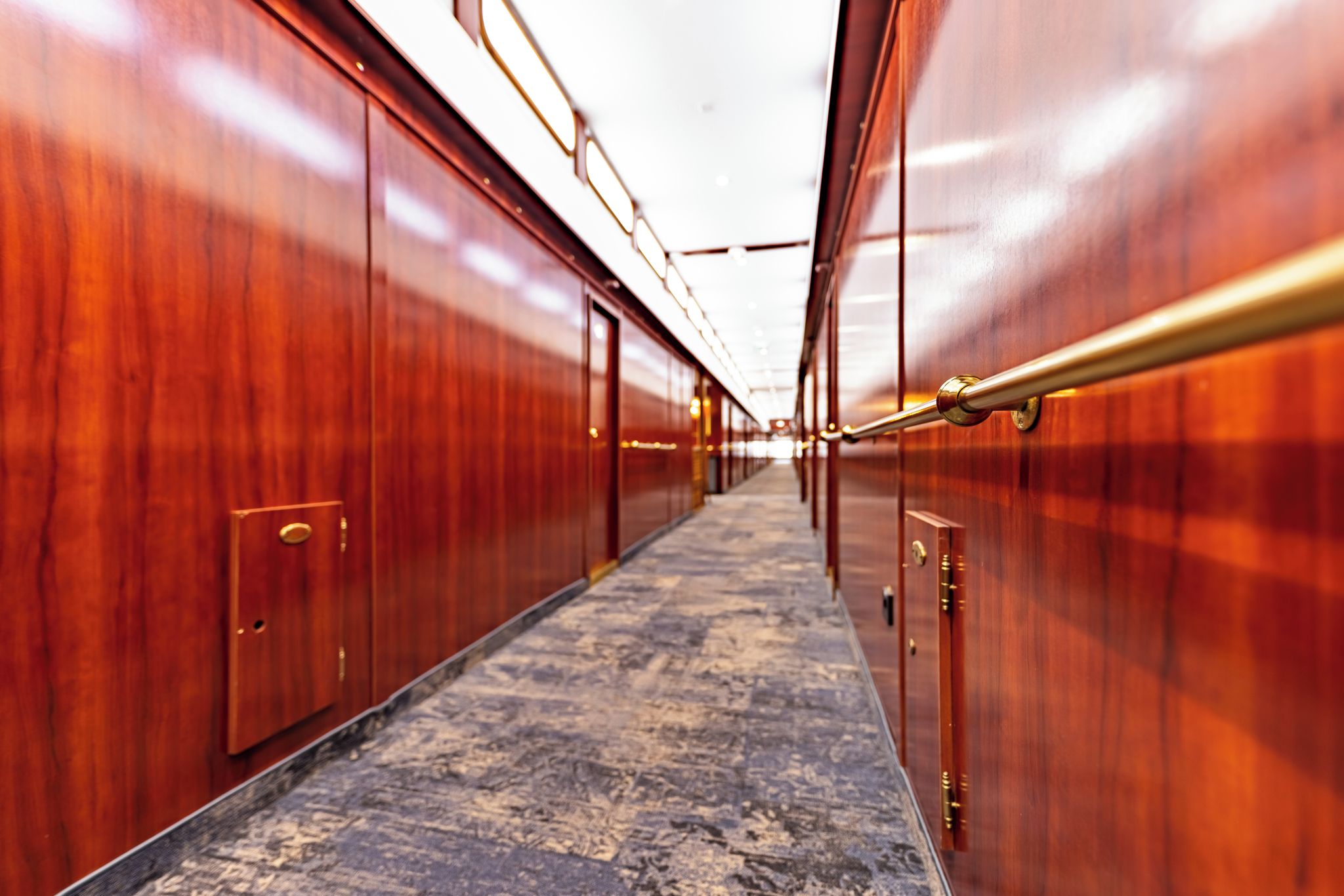 A corridor with wooden doors and a marble floor, leading to a bright room.