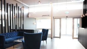 A modern lobby with a blue sofa, two armchairs, a coffee table, and pendant lights. A sign indicates a breakfast area.