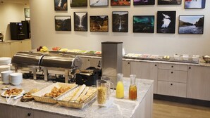 A buffet area with various food items, a coffee station, and a wall decorated with landscape photographs.