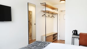 A modern hotel room with a bed, a TV, a wooden bench, a coat rack, and a coffee table.