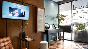 Ein Hotel-Rezeptionsbereich mit einer braunen Ledersofa, einem Fernseher, der eine Willkommensnachricht zeigt, einer Speisekarte für Snacks und Getränke sowie Blick auf die Straße.