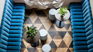 Eine moderne Sitzgruppe mit blau gepolsterten Bänken, einem Holzboden mit geometrischem Muster und runden Tischen mit Blumentöpfen.