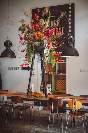 A dining area with a black pendant lamp, a floral centerpiece, and a wall with a sign that reads 'GAME ON!!'. - Hotel Emma (Rotterdam)
